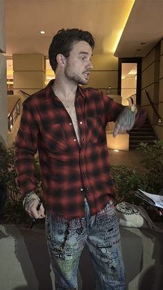 a man standing in front of a building with his hands out to the side while wearing ripped jeans and a flannel shirt