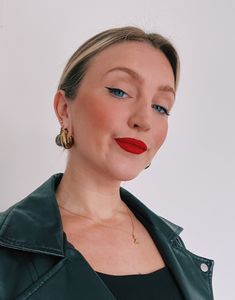 a woman with blue eyes and red lips wearing a green jacket, gold hoop earrings