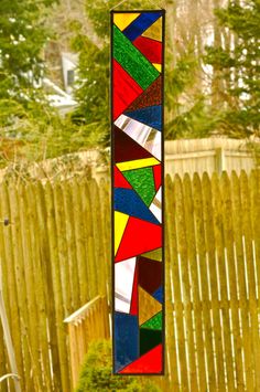 a colorful stained glass window hanging from a wooden fence in front of a garden area