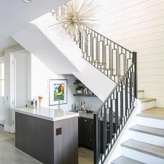 an open staircase leading up to a kitchen and living room with white walls, wood flooring, and stainless steel handrails