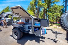 an off road camper parked in the middle of a parking lot with people looking at it