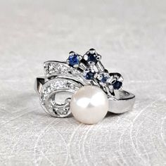 a white pearl and blue sapphire ring on a silver surface with an embellishment in the middle