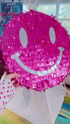 a person holding up a pink sequinized smiley face pillow with hearts on it