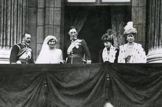 black and white photograph of four people on balcony with drapes in front of them