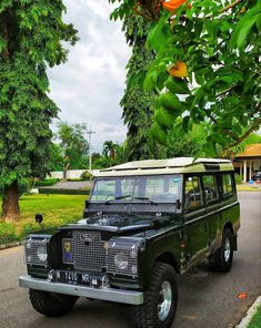 a green land rover is parked on the side of the road in front of some trees