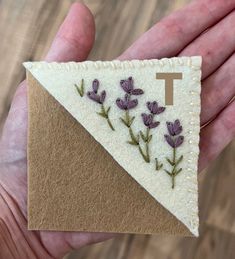 a hand holding a small piece of felt with flowers on it and the letter t