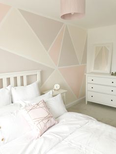 a white bed sitting under a pink lamp next to a dresser