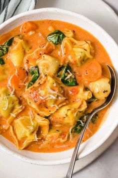 a white bowl filled with tortellini and spinach soup next to a spoon