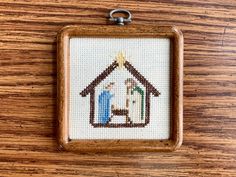 a cross stitch nativity ornament hanging from a wooden frame