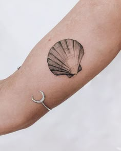 a small tattoo on the arm of a woman with a shell and crescent moon in it