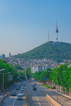 cars are driving down the street in front of a hill with a city on it