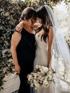 two women standing next to each other in front of a wall covered with greenery