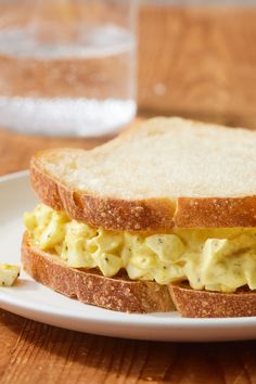 an egg salad sandwich on a white plate with a glass of water in the background