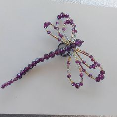 a purple beaded dragonfly brooch sitting on top of a white table next to a pair of scissors