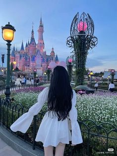 a woman standing in front of a castle at disneyland world with her back to the camera