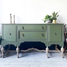 an old dresser painted green with white trim and some potted plants sitting on top