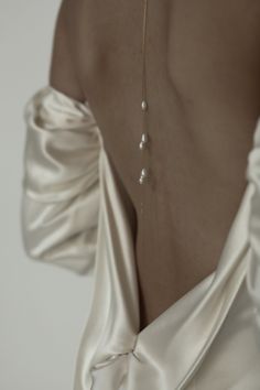 the back of a woman wearing a white dress with pearls on it's neck