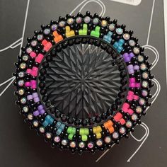 a colorful beaded brooch sits on top of a black card board with white writing