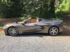 a grey sports car parked on gravel near trees