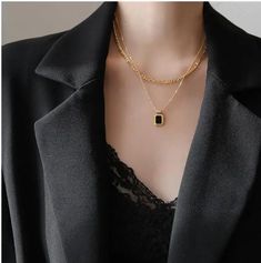 This necklace embodies a harmonious blend of textures and colors, with layers of lustrous gold stainless steel chains that elegantly cascade and culminate in a striking bezel-set black or white stone pendant. The contrast between the radiant gold and the deep black stone exudes a sense of intrigue and luxury, making it an ideal accessory for elevating any ensemble. With its versatile design and meticulous craftsmanship, this necklace becomes a symbol of refined elegance and modern style.Stainles Black Pendant Necklace With Chain, Elegant Black Necklaces With Adjustable Chain, Elegant Metal Chain Necklace With Square Pendant, Elegant Double Chain Pendant Necklace, Elegant Pendant Necklace With Double Chain, Elegant Gold Chain Layered Necklace, Elegant Black Jewelry With Adjustable Chain, Elegant Layered Gold Chain Necklace, Black Metal Pendant Chain Necklace