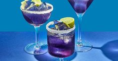 two purple cocktails with lemon wedges and garnishes on the rim