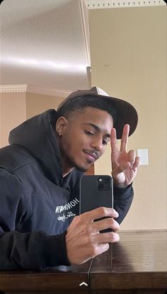 a young man sitting at a table using his cell phone and making the peace sign