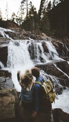 a man and woman standing in front of a waterfall with backpacks on their shoulders