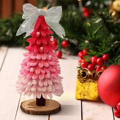 a small pink christmas tree sitting on top of a wooden table next to a red ornament