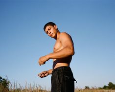 a shirtless man holding a frisbee in his right hand and looking down