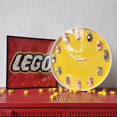 a clock made out of legos sitting on top of a red table next to a wall