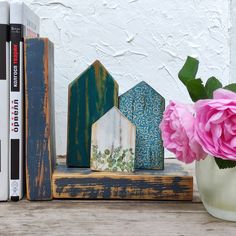 a vase with pink flowers next to two books on a wooden shelf and a bookend