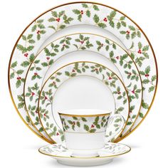 a white and gold christmas dinnerware set with holly designs on the rims,