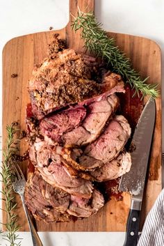 sliced roast beef on cutting board with knife and rosemary sprig