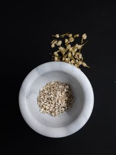 a white bowl filled with oatmeal next to dried flowers on a black surface