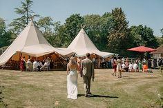 a bride and groom are walking through the grass in front of tippy - top tents