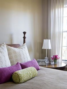 a bed with purple and green pillows on top of it next to a window in a bedroom