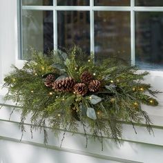 a window sill with pine cones and greenery hanging from it's side