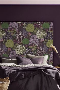 a bed with purple and green wallpaper next to a basket filled with pillows on top of it