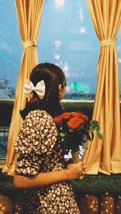 a woman is looking out the window with flowers in front of her and an orange rose behind her