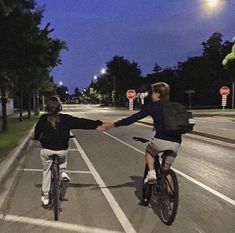 two people riding bikes down the street holding hands