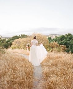 a woman in a white dress is walking through tall grass