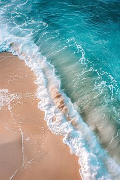 an ocean wave rolls in to the beach with blue water and sand on it's shore