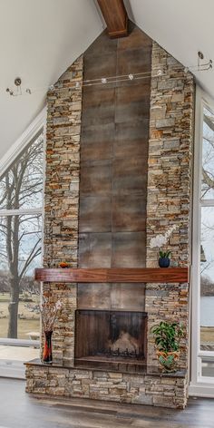 a large stone fireplace in the middle of a living room with wood flooring and vaulted ceiling