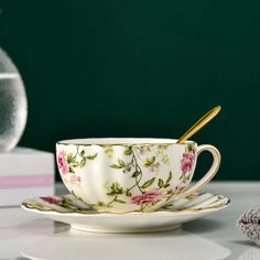 a tea cup and saucer sitting on a table next to a vase with flowers