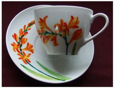 a white cup and saucer with orange flowers painted on the side, sitting on a red table cloth