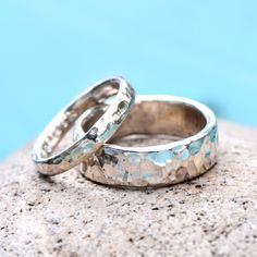 two silver wedding rings sitting on top of a rock next to each other with blue water in the background