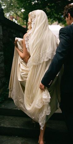 a man and woman dressed in wedding attire walking down the stairs together, both wearing veils