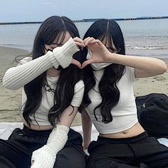 two young women sitting on top of a bed next to each other near the ocean