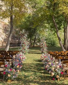 an outdoor ceremony setup with wooden chairs and flowers on the aisle, surrounded by trees