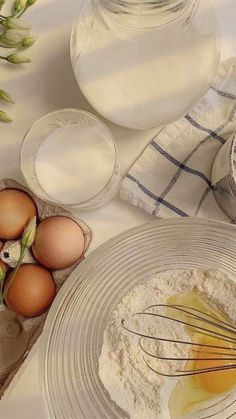 eggs and flour in bowls on a white tablecloth next to an empty glass bottle